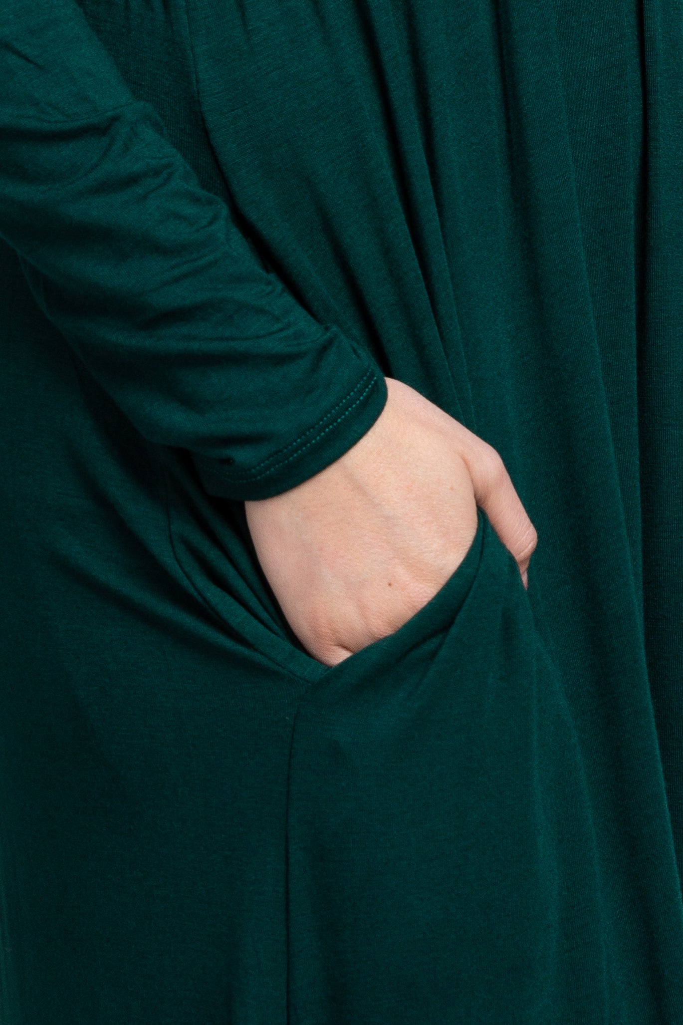 close-up of a woman's hand in the pocket of a dark green long sleeve dress