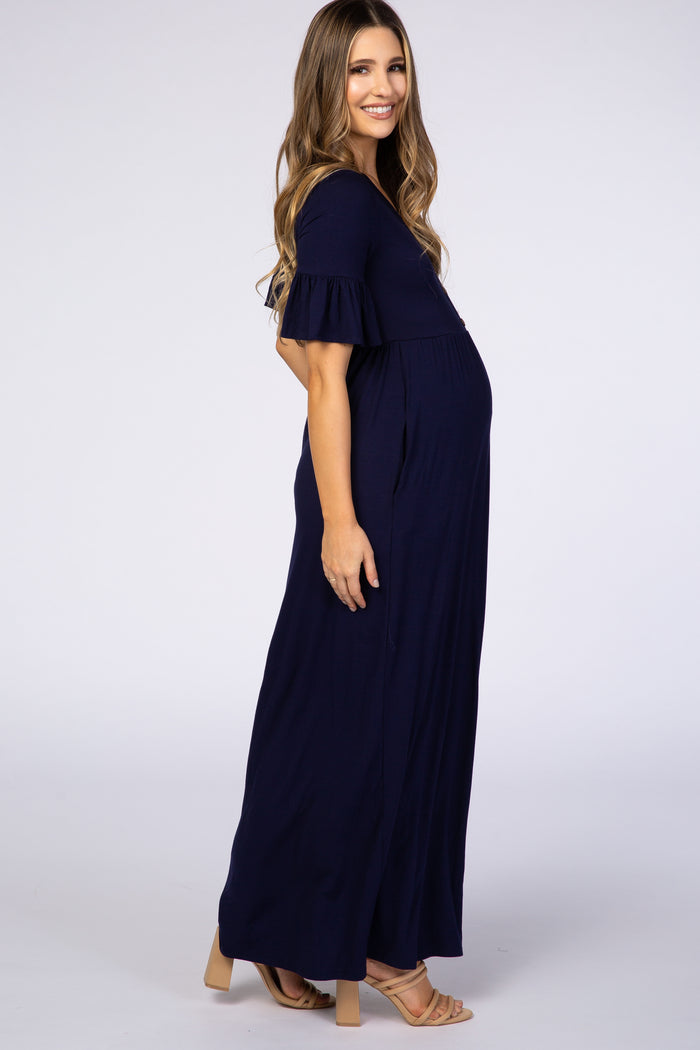 Pregnant woman wearing a navy blue short sleeve maternity maxi dress with ruffle sleeves and tan heels