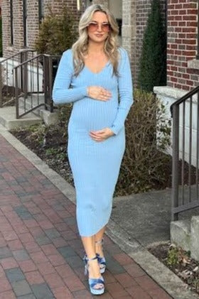 woman wearing a light blue ribbed maternity dress and holding her baby bump while walking outside