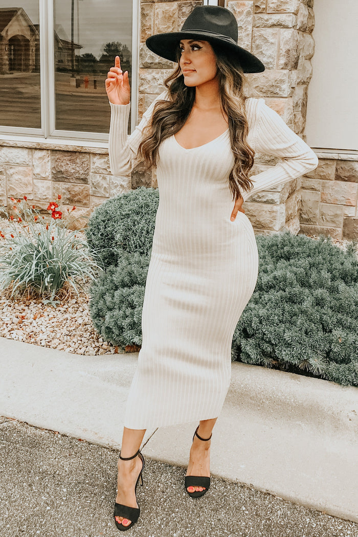 woman wearing a ribbed cream knit maxi dress and a black wide-brimmed hat, posing outdoors with a stylish stance