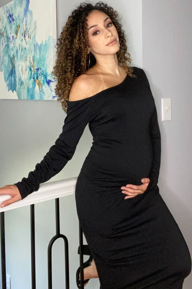 woman wearing a black off-shoulder maternity dress and holding her baby bump