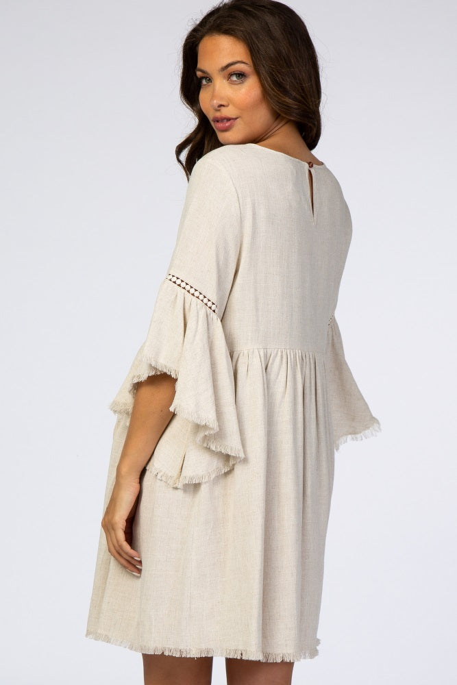 woman wearing a beige maternity dress with bell sleeves and a keyhole back detail