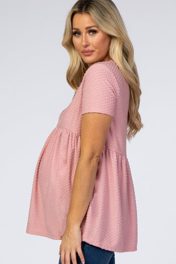 woman wearing a light pink short sleeve maternity top with textured dot detail and a visible baby bump