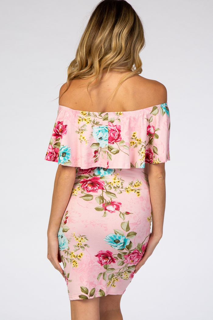 Back view of a woman wearing a pink floral off-the-shoulder maternity dress with a ruffled neckline.