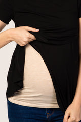 woman wearing a black maternity top, lifting it to reveal her baby bump with a beige undershirt beneath