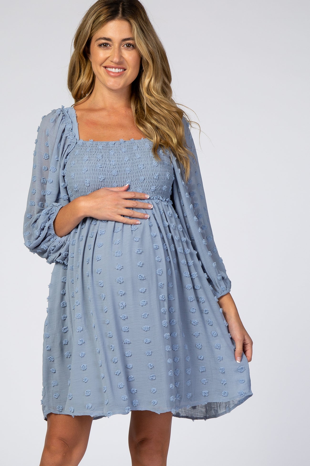 woman wearing a light blue maternity dress with a smocked bodice and puff sleeves, holding her baby bump