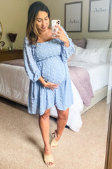 woman wearing a light blue maternity dress with puff sleeves and holding her baby bump in a bedroom setting
