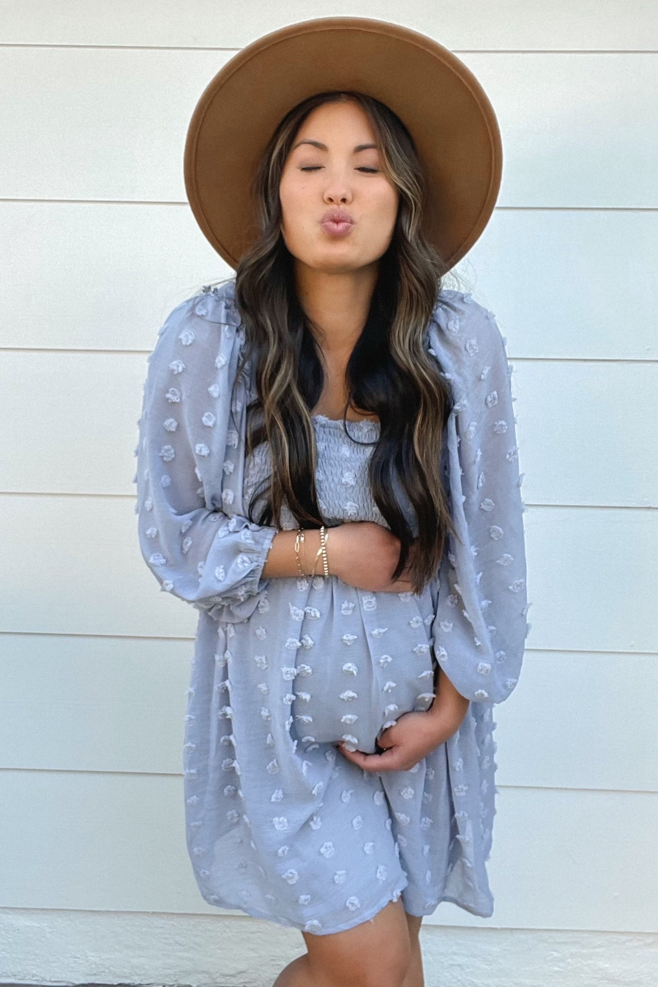 woman wearing a gray maternity dress with puff sleeves and holding her baby bump, accessorized with a wide-brimmed hat