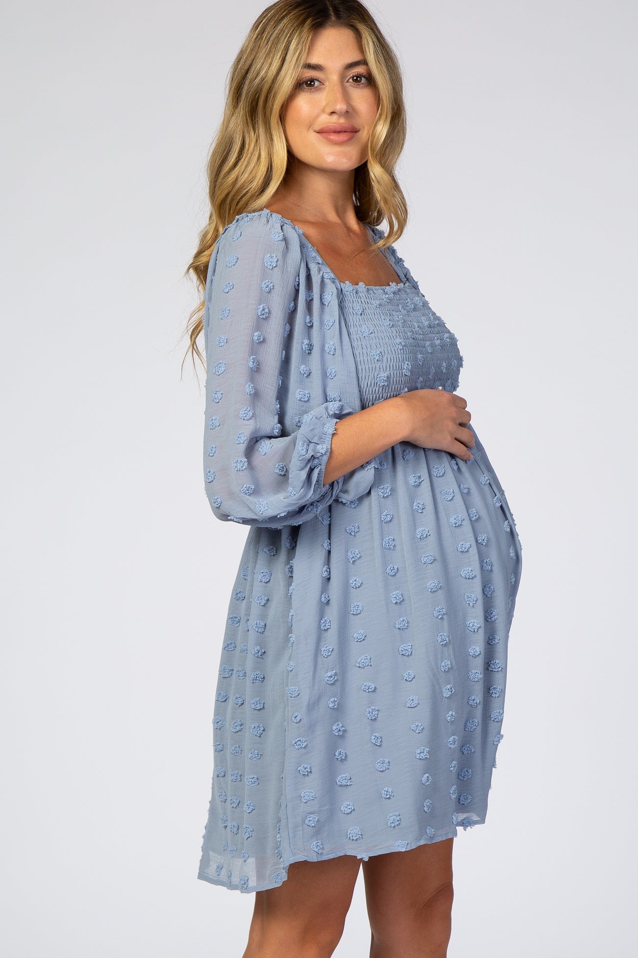 woman wearing a light blue maternity dress with textured dots and a smocked bodice, showcasing her baby bump