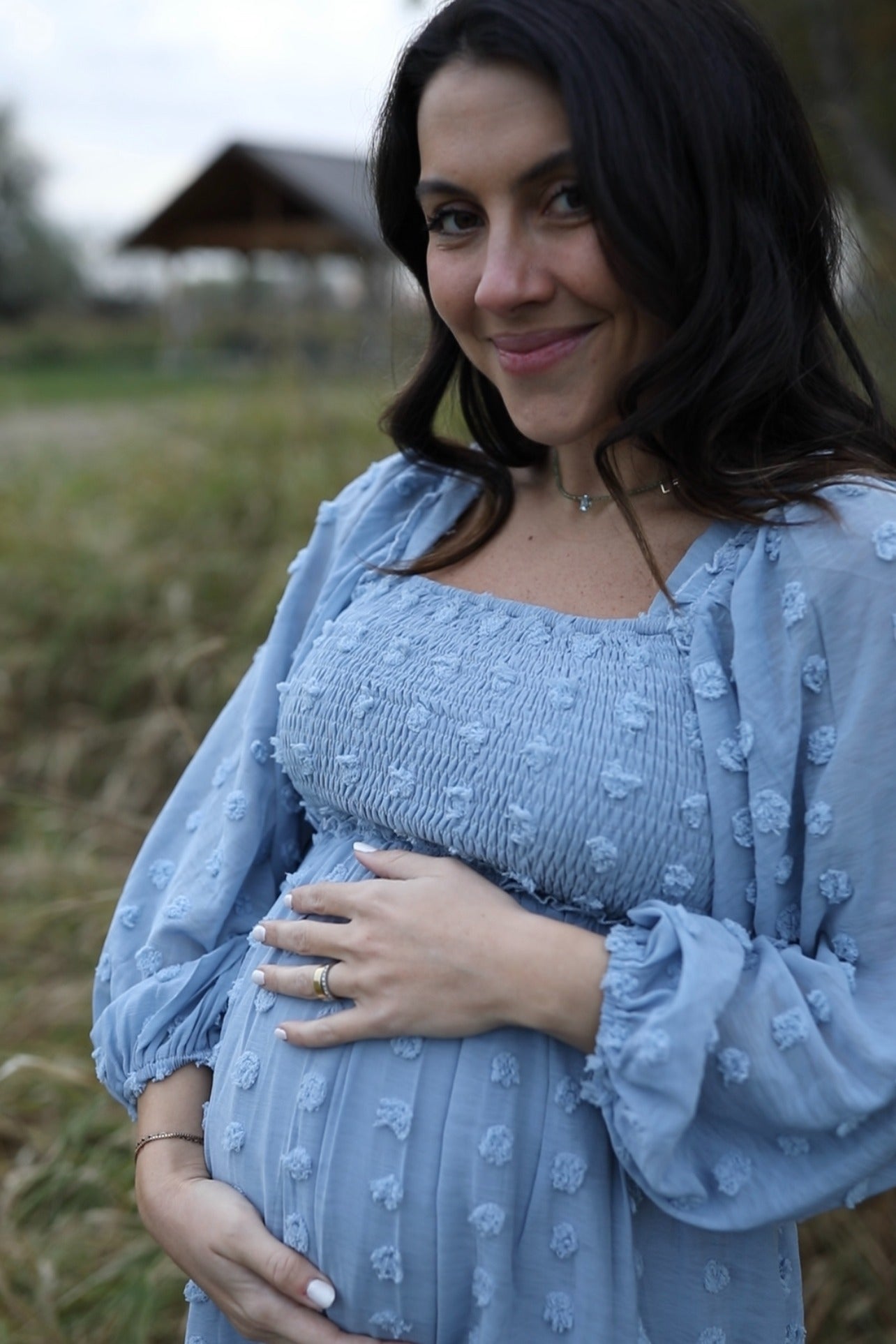 woman wearing a light blue maternity dress with textured details and puff sleeves, holding her baby bump
