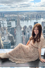 woman sitting on an observation deck wearing a light beige floral maxi dress with short sleeves and a pleated skirt