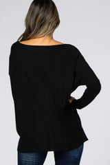 woman wearing a black oversized sweater with a wide neckline, styled with dark blue jeans