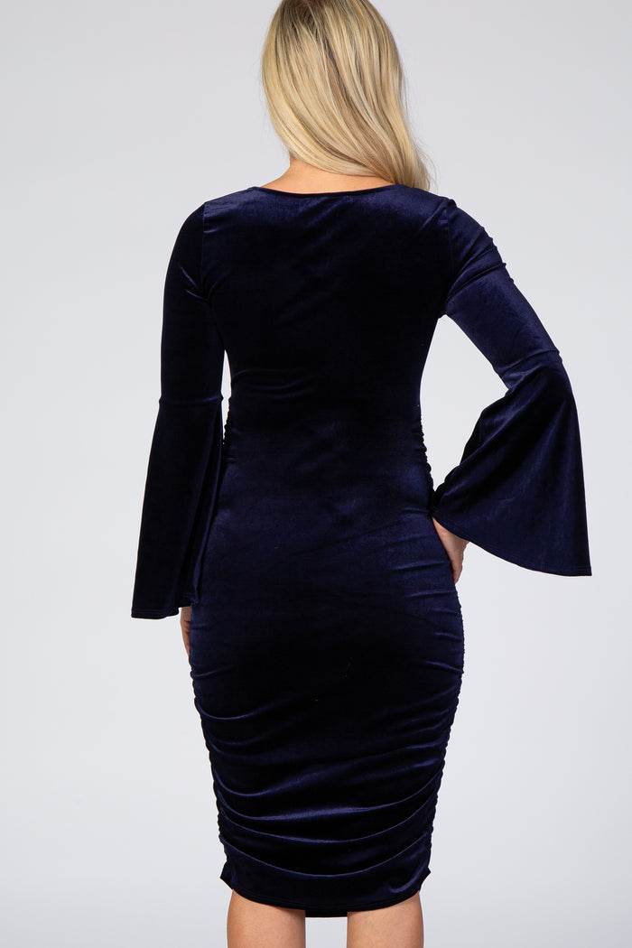 woman wearing a navy blue velvet maternity dress with bell sleeves and ruched detailing at the back