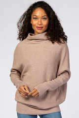 woman wearing a light brown oversized sweater with a cowl neck and long sleeves, paired with blue jeans