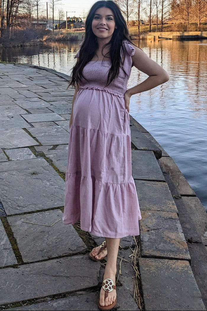 woman wearing a pink maternity maxi dress with flutter sleeves and a baby bump by the water
