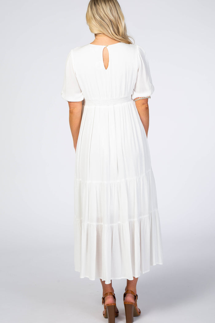 woman wearing a white maternity maxi dress with short puff sleeves and a tiered skirt, showing a keyhole back detail