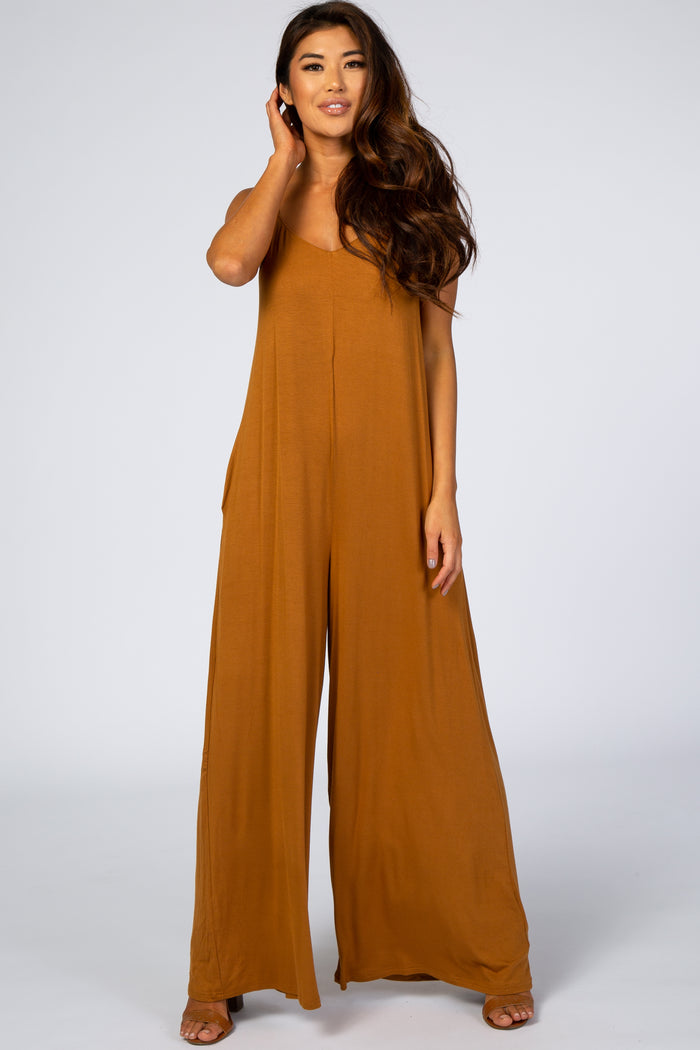 woman wearing a camel colored wide leg maternity jumpsuit with spaghetti straps and pockets