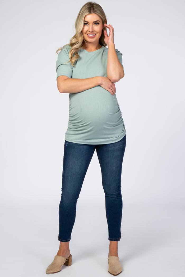 woman wearing a mint green short sleeve maternity top and dark blue skinny jeans, showing her baby bump