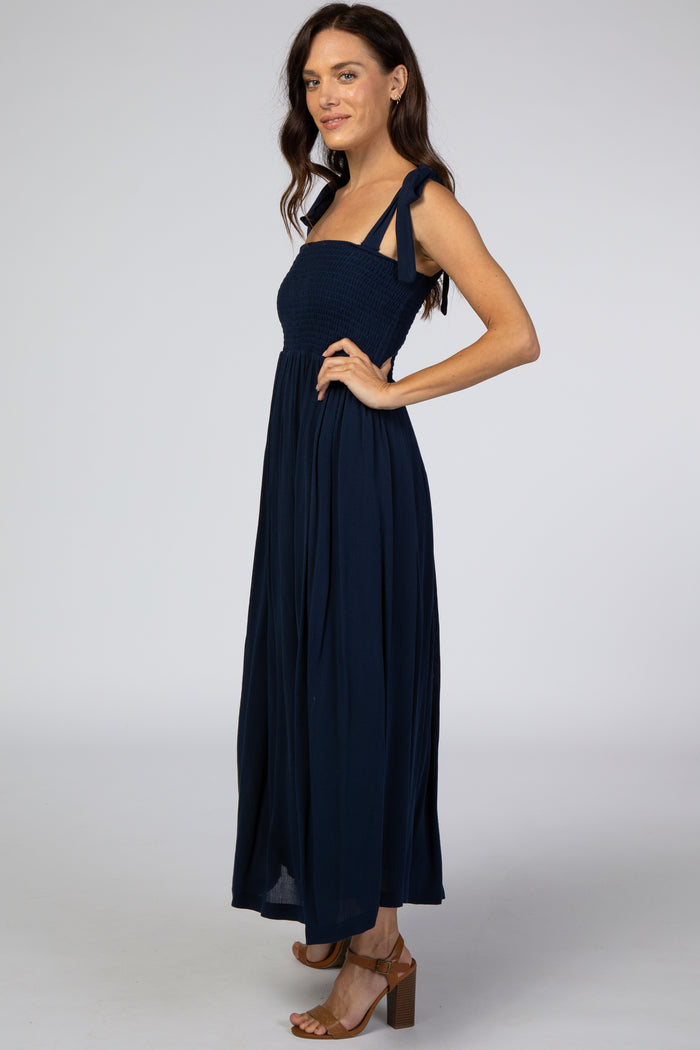 woman wearing a navy blue maxi dress with smocked bodice and tie straps, posing sideways