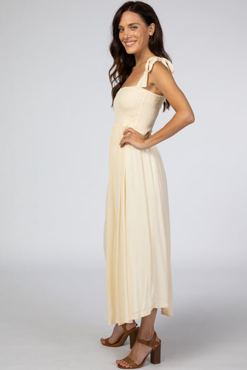 woman wearing a light yellow maxi dress with a smocked bodice and tie straps, standing in profile