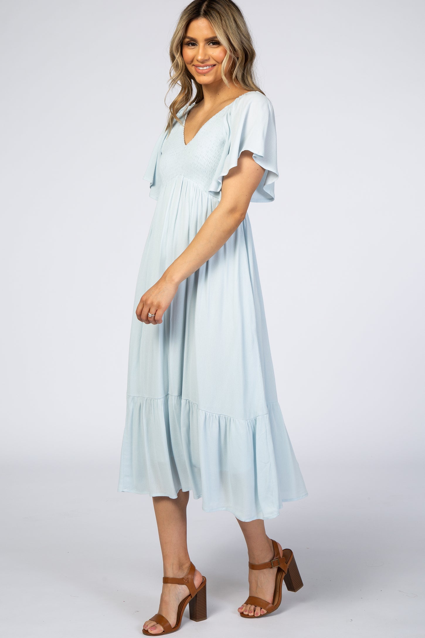 woman wearing a light blue v-neck flutter sleeve midi dress with a tiered hem and brown block heel sandals