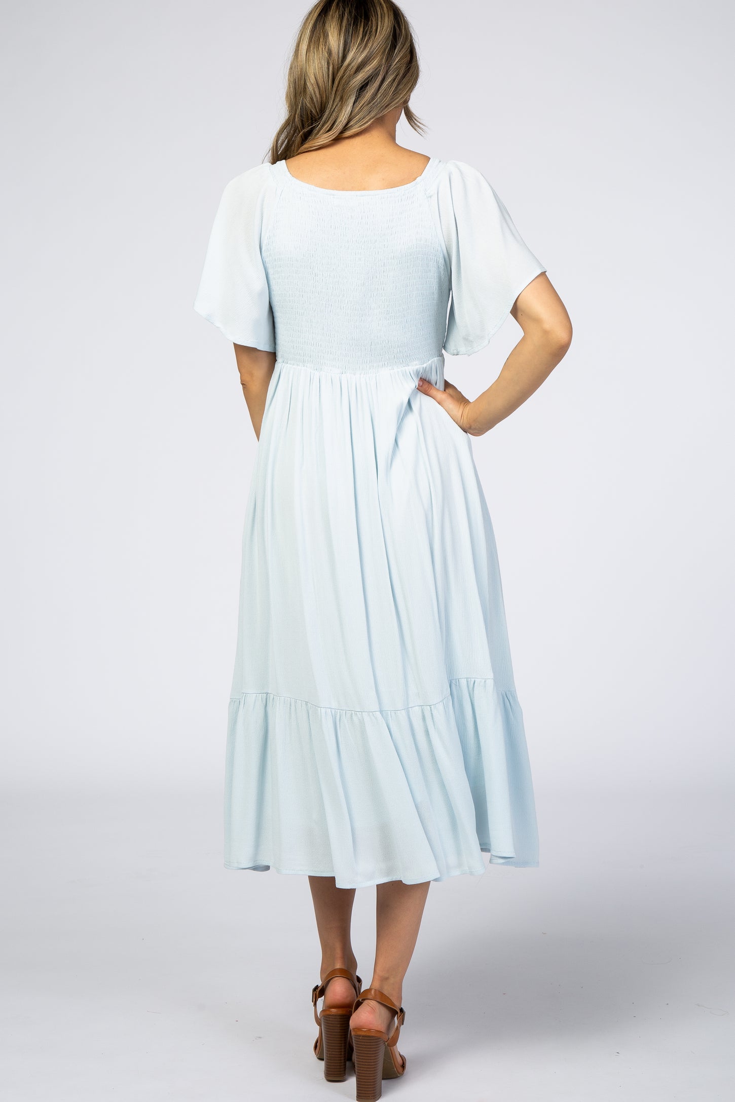 woman wearing a light blue smocked back midi dress with flutter sleeves and a tiered skirt