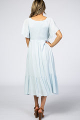woman wearing a light blue smocked back midi dress with flutter sleeves and a tiered skirt