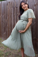woman wearing a green floral print maternity dress, gently holding her baby bump against a wooden fence backdrop