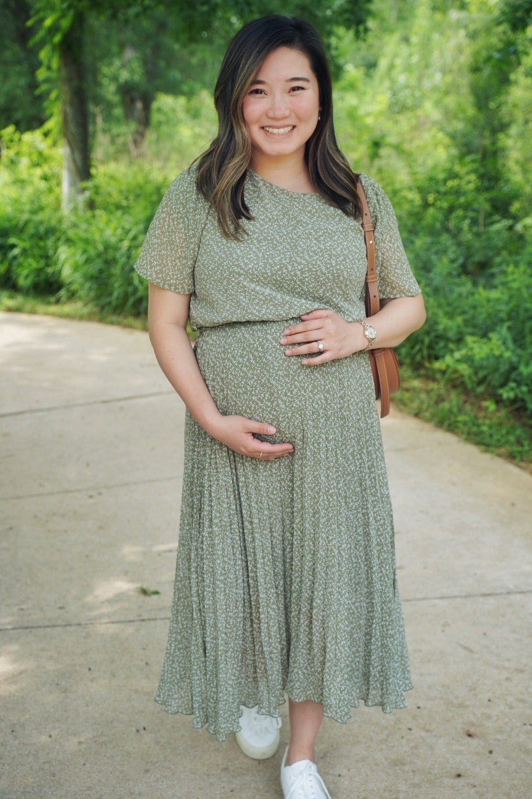 Smiling pregnant woman in a green floral maternity dress posing on a park path