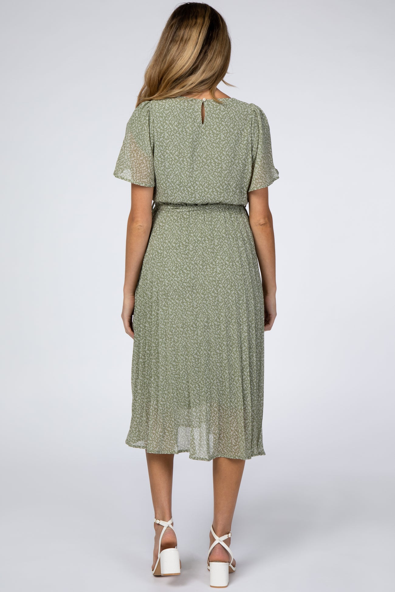 woman wearing a green floral maternity dress with short sleeves and a cinched waist, showing her baby bump from the back