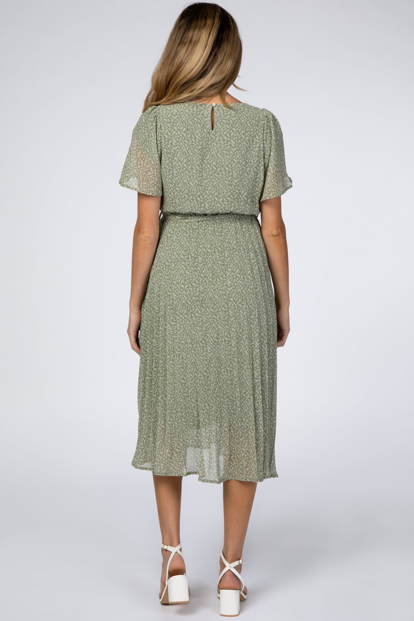 woman wearing a green floral maternity dress with short sleeves and a cinched waist, showing her baby bump from the back