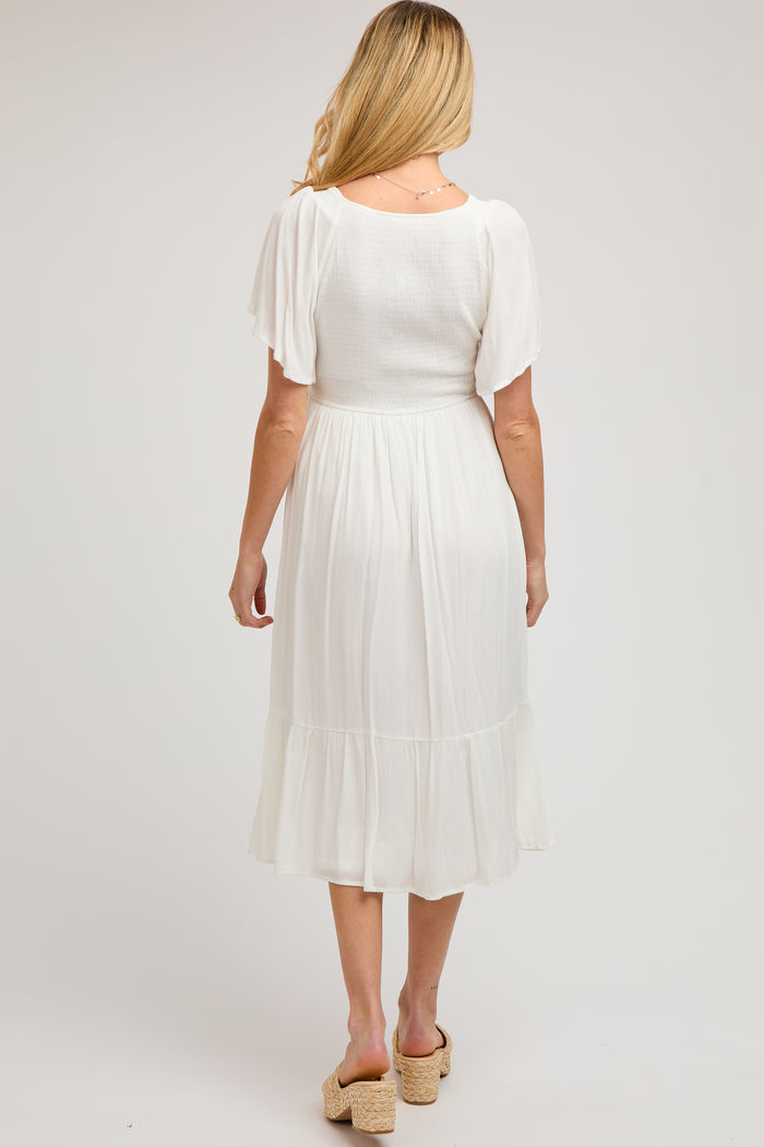 woman wearing a white maternity maxi dress with short flutter sleeves and a tiered ruffle hem, showing her back