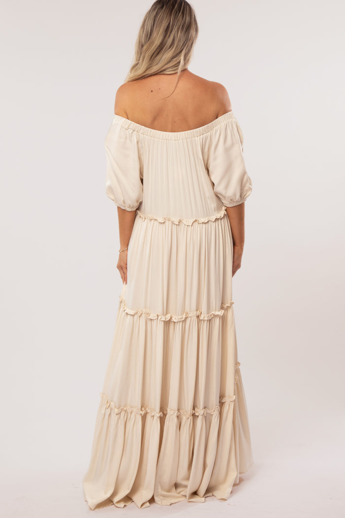woman wearing a beige off-the-shoulder maternity dress with puff sleeves and tiered design from the back