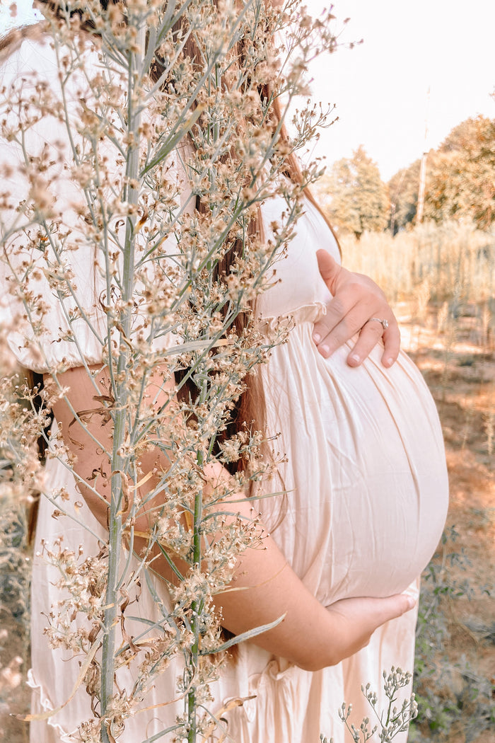 woman wearing a light pink maternity dress and holding her baby bump among plants