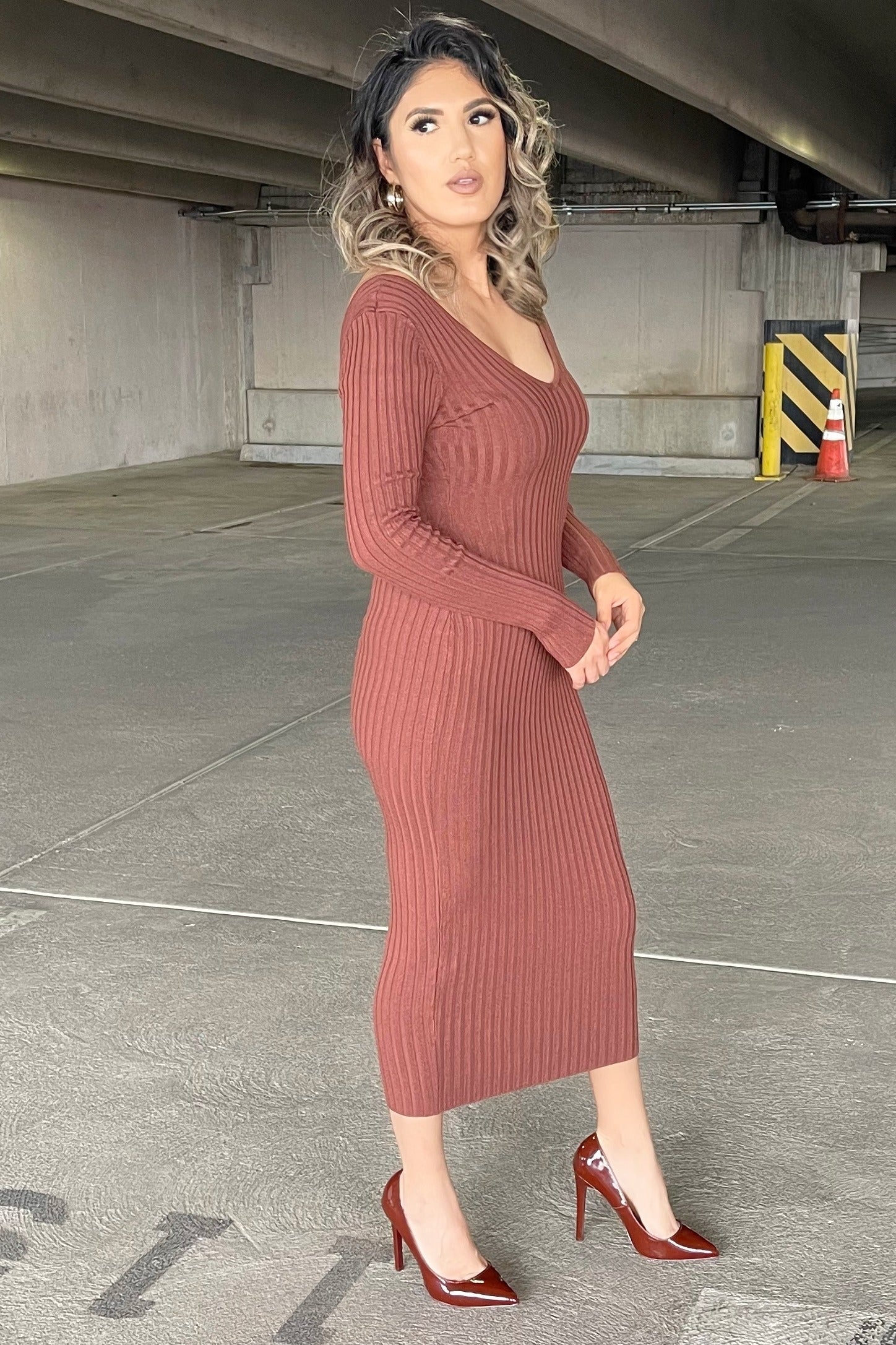 woman in a long sleeve ribbed knit midi dress in rust brown with matching high heel pumps in a parking garage