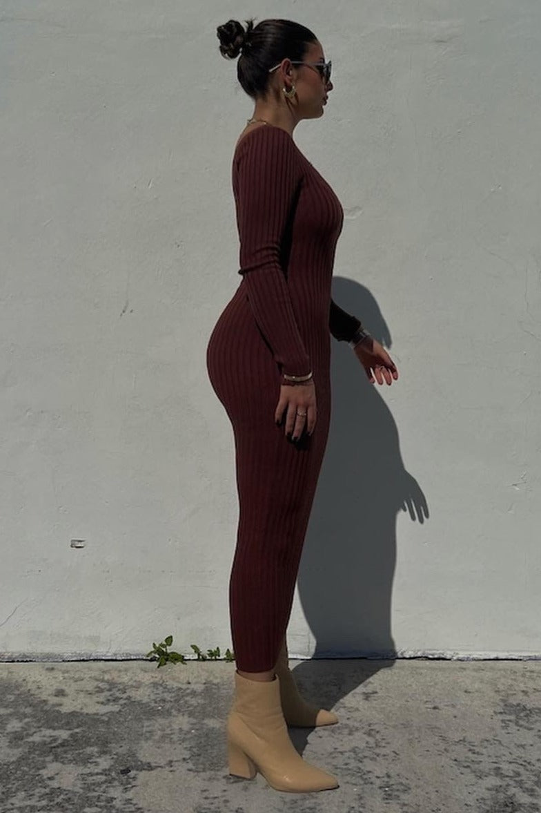 woman wearing a fitted burgundy ribbed long sleeve dress and beige ankle boots, standing against a light wall