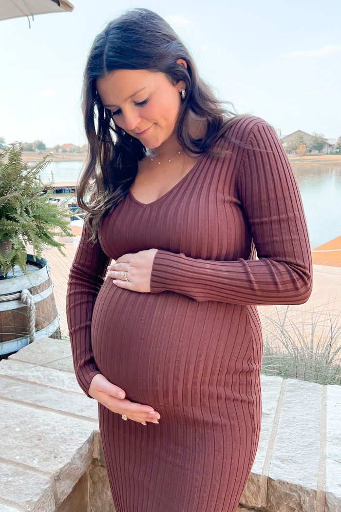 woman wearing a brown ribbed long sleeve maternity dress, gently cradling her baby bump