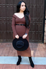 woman wearing a fitted rust ribbed midi dress with long sleeves and a belted waist, holding a black wide-brim hat