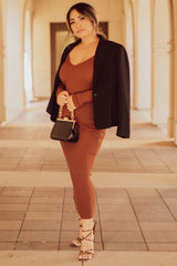 woman wearing a rust ribbed knit dress with a blazer and strappy heels, holding a black crossbody bag