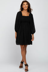 woman wearing a black puff sleeve dress with a textured fabric and flared skirt, standing and smiling