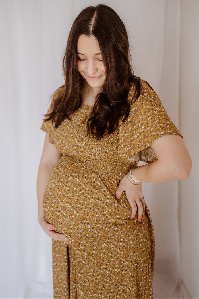 woman wearing a mustard yellow floral maternity dress and cradling her baby bump