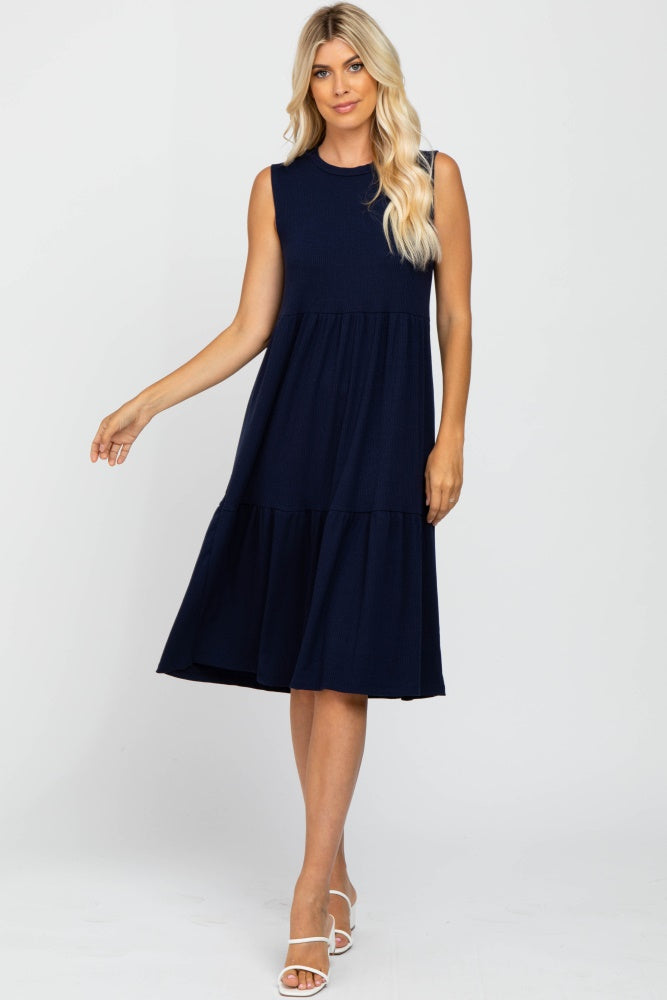 blonde woman wearing a sleeveless navy blue tiered midi dress and white strappy sandals