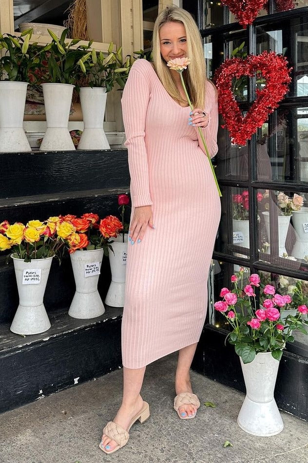 woman wearing a light pink ribbed knit midi dress with long sleeves, standing amidst flowers and holding a flower