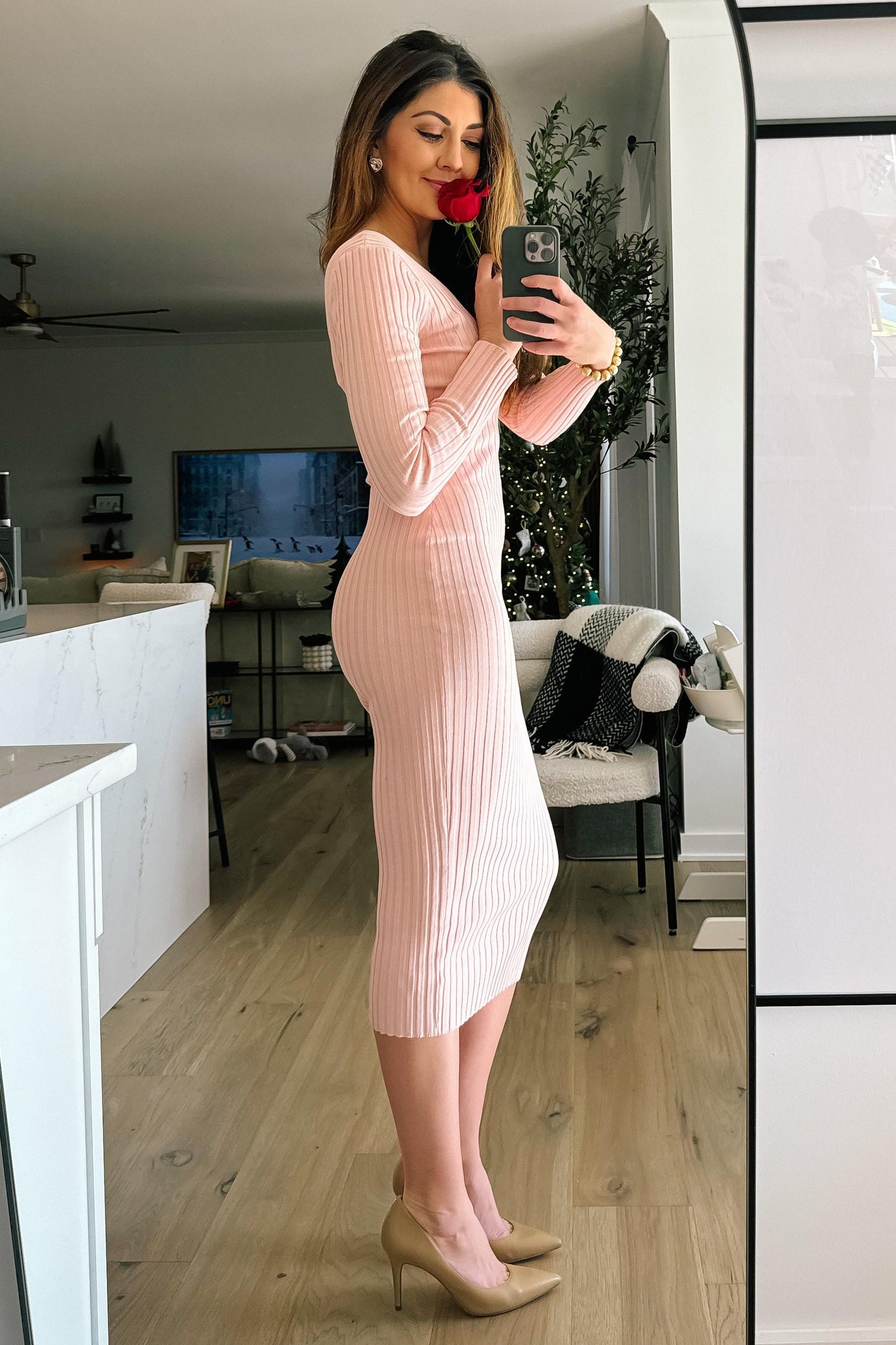 woman wearing a pink ribbed midi dress and holding a rose, standing in a well-decorated living space