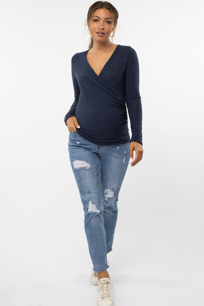 woman wearing a navy blue long sleeve wrap maternity top and distressed jeans, with a visible baby bump