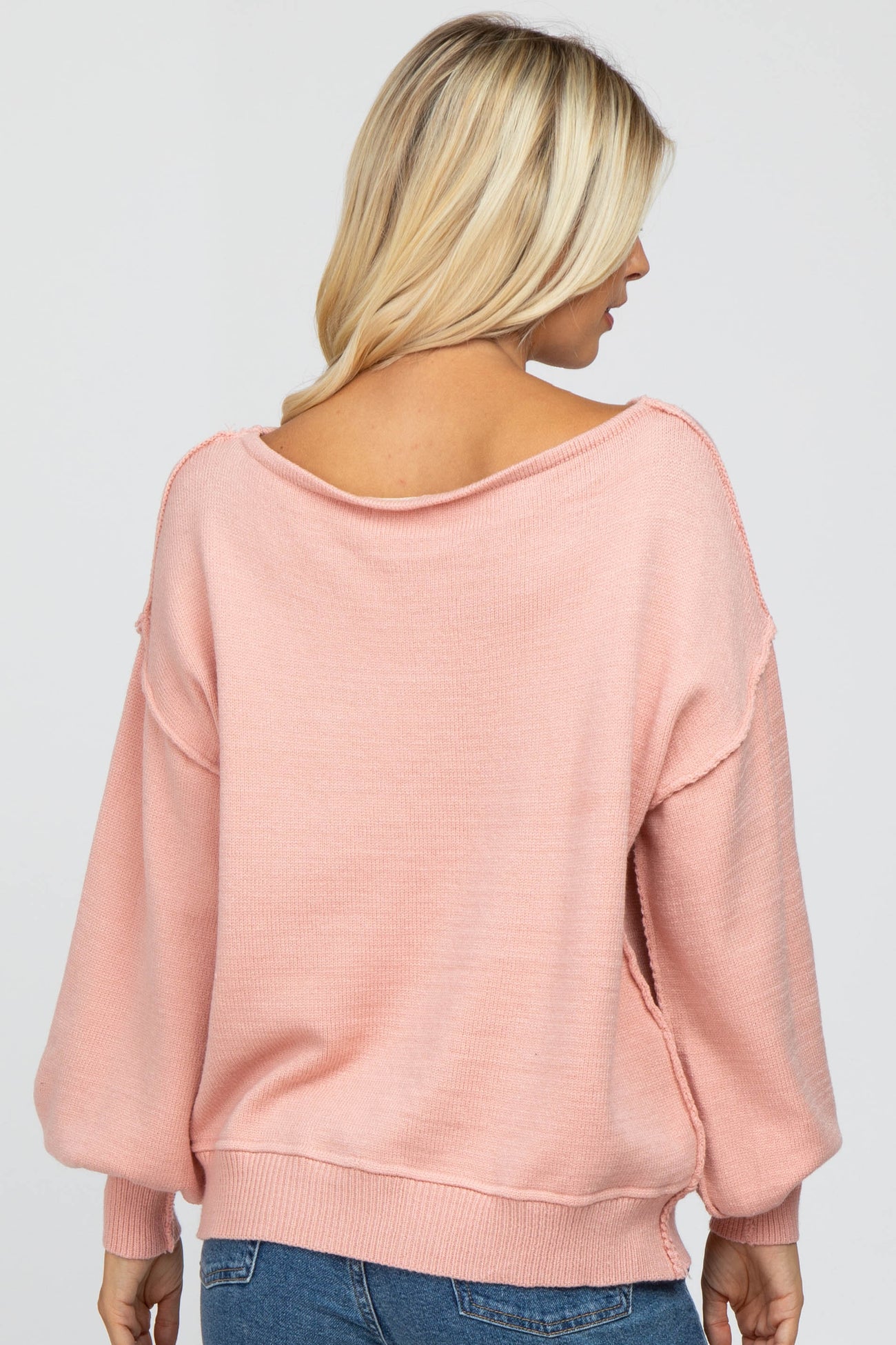 woman wearing a light pink oversized sweater with a wide neckline and side slits, viewed from the back