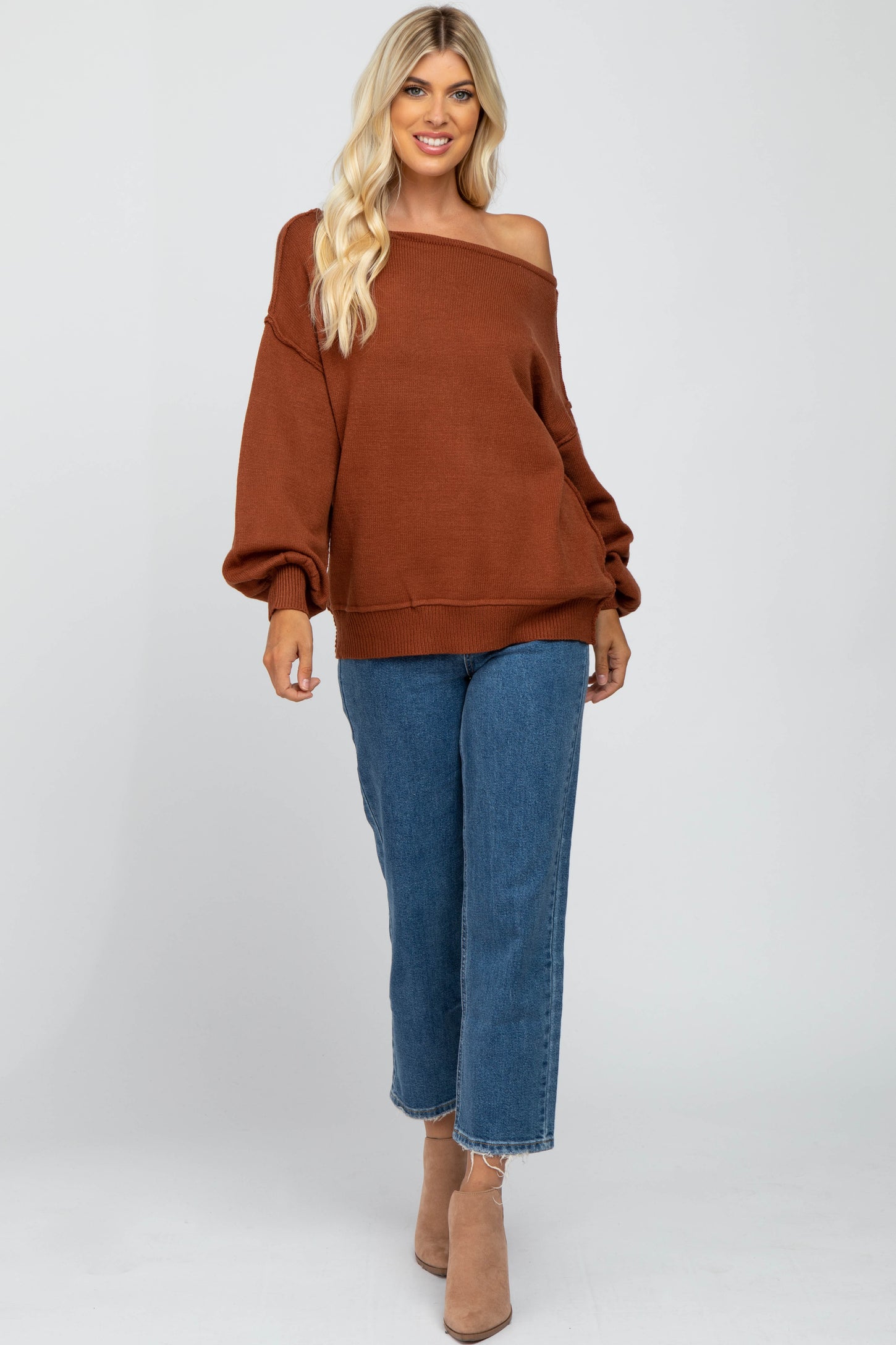 woman wearing an oversized rust colored off-the-shoulder sweater with balloon sleeves and blue cropped wide-leg jeans