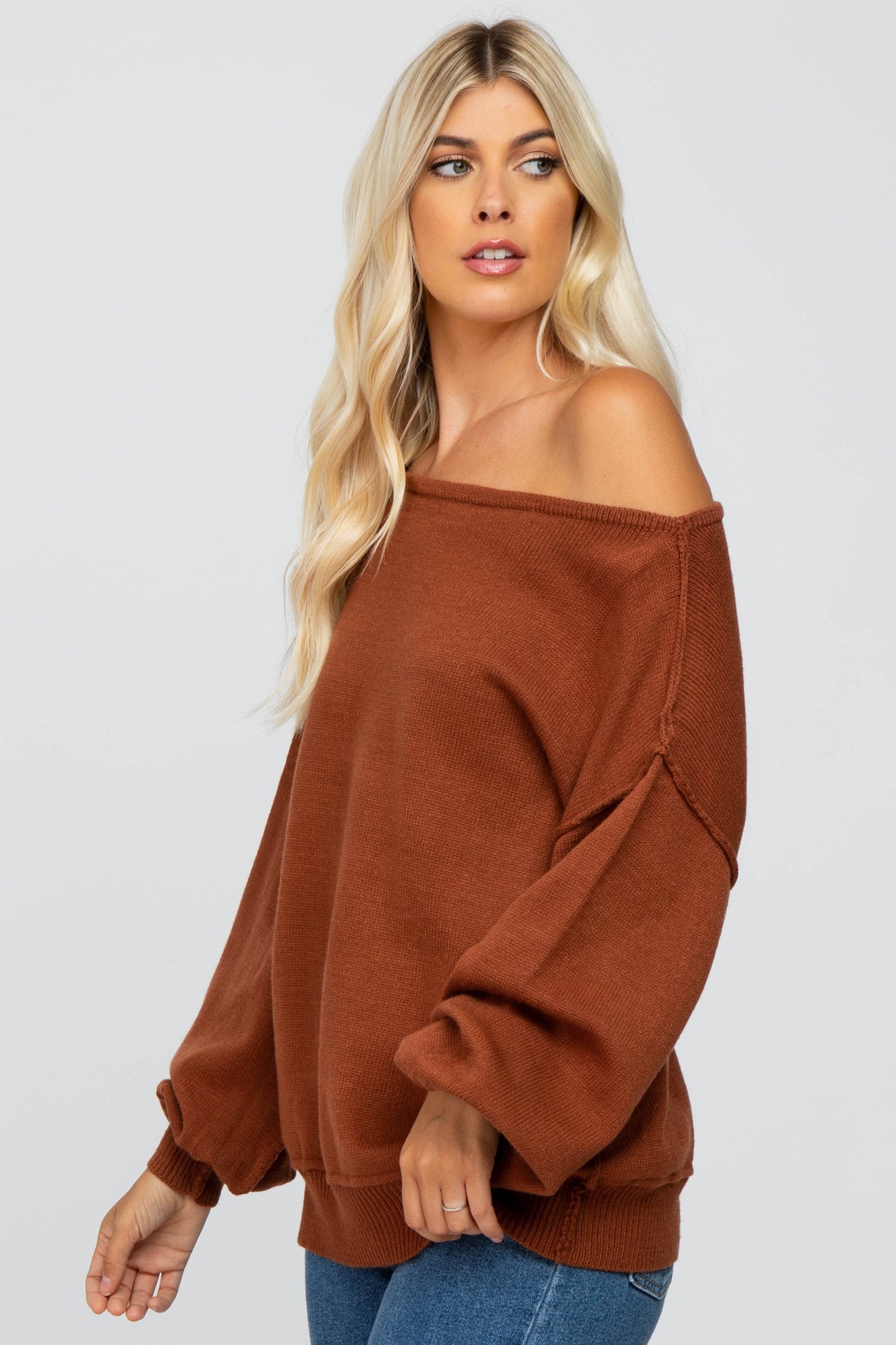 woman wearing a rust-colored off-the-shoulder sweater with balloon sleeves and a relaxed fit