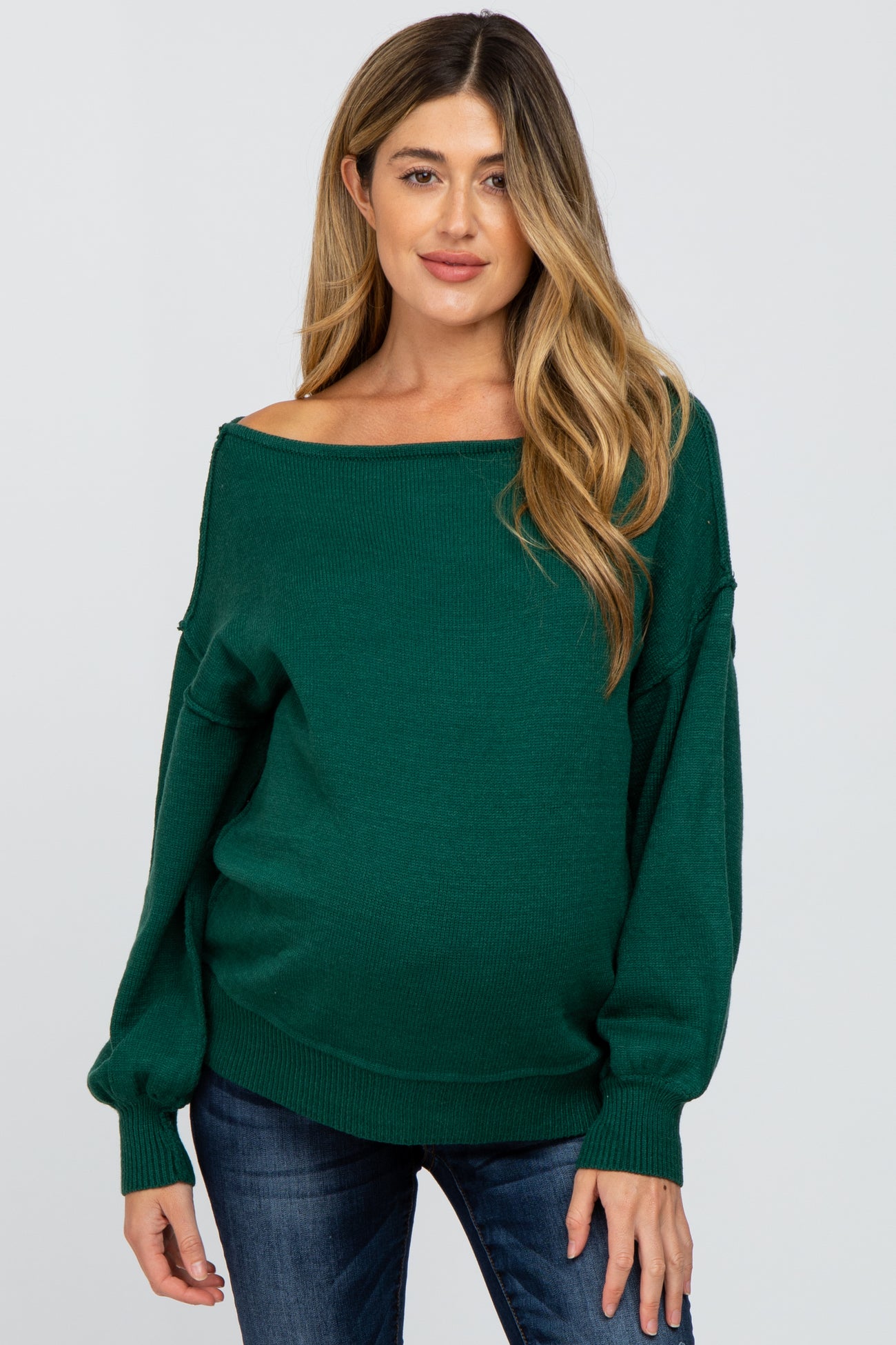 woman wearing a dark green off-the-shoulder maternity sweater and showing her baby bump