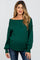 woman wearing a dark green off-the-shoulder maternity sweater and showing her baby bump